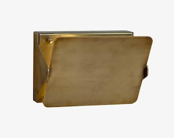 May include: A rectangular, brass-colored wall-mounted light fixture with a hinged, angled front panel. The fixture is open, revealing the interior. The metal has a brushed finish, and the design is minimalist.