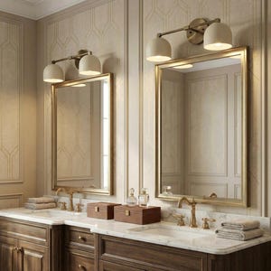 May include: A bathroom vanity with two mirrors, each framed in gold. Above each mirror are two cream-colored sconces. The vanity has a marble countertop, dark wood cabinets, and gold fixtures. Decorative boxes and perfume bottles are on the countertop.