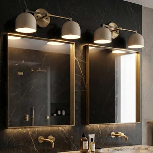 May include: Two square mirrors with gold frames are mounted on a dark marble wall. Above each mirror is a light fixture with three beige dome-shaped lights. The bathroom features gold faucets and fixtures, creating a luxurious aesthetic.