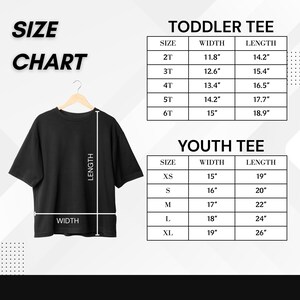 May include: A black t-shirt displayed on a hanger, with a size chart for toddler and youth tees. The chart lists sizes, widths, and lengths in inches. The text "SIZE CHART" is at the top left.
