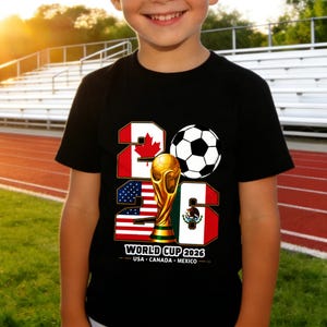 May include: Black t-shirt with a graphic design for the 2026 World Cup. The design includes the numbers 2026, a soccer ball, the World Cup trophy, and flags of the USA, Canada, and Mexico. The text "WORLD CUP 2026" is also included.