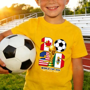 May include: A yellow t-shirt featuring a soccer ball and the text "2026 WORLD CUP" with flags of USA, Canada, and Mexico. The shirt is worn by a person holding a soccer ball.