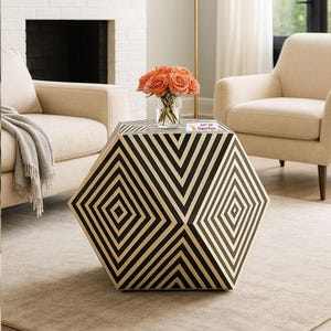 May include: A hexagonal side table with a striking black and gold geometric design. The table holds a vase of orange roses and a small book. The table is in a living room setting, with a rug and chairs.