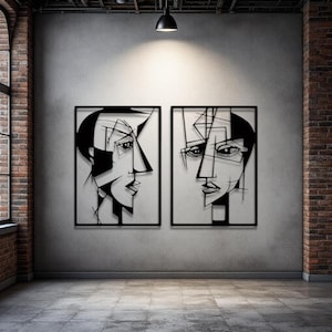 Op de afbeelding: Twee ingelijste zwarte metalen wandkunstwerken. Elk heeft een gestileerd, abstract gezichtsprofiel. Het kunstwerk staat tegen een grijze muur, met een bakstenen muur en raam zichtbaar aan de linker- en rechterkant.