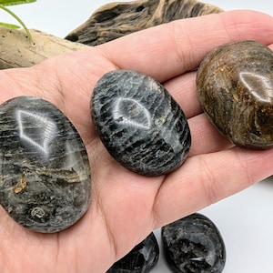 May include: Three smooth, oval-shaped stones with a dark gray and brown marbled pattern. The stones are polished and have a glossy finish.