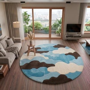 May include: A large circular area rug featuring a layered, abstract cloud pattern in shades of sky blue, cream, and dark brown. The rug is placed in the center of a living room with hardwood floors, a beige sofa, and a wooden dining table set.