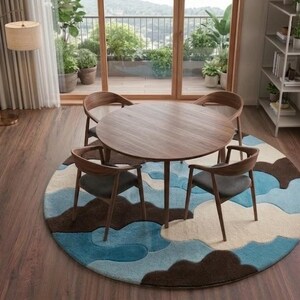 May include: A round wooden dining table with four matching chairs featuring dark gray upholstered seats. The furniture set is placed on a large circular area rug with a layered, abstract pattern in shades of blue, brown, and cream.