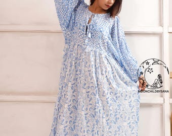 May include: A long, flowing dress with a blue and white floral pattern. The dress features long sleeves, a tie-neck, and a tiered skirt. The dress is made of a lightweight fabric, perfect for warm weather. The dress is from Moonchildbysana.