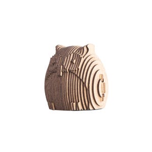 May include: A wooden owl-shaped box, constructed from layered, laser-cut wood. The owl has a rounded body and a hinged door. The natural wood tones create a warm, earthy aesthetic. The design is detailed and three-dimensional.