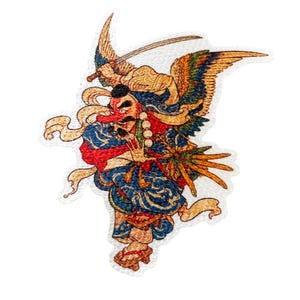 May include: An embroidered patch featuring a Tengu figure with a long red nose, black hair, and wings. The figure wears a blue patterned robe, holds a sword above its head, and stands on wooden sandals. The design includes yellow, blue, and red.