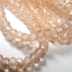May include: A strand of iridescent pink glass beads. The beads are faceted and have a slightly irregular shape.