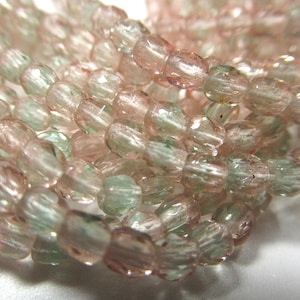 May include: A strand of faceted glass beads in shades of pink and green. The beads are translucent and have a slightly iridescent finish.