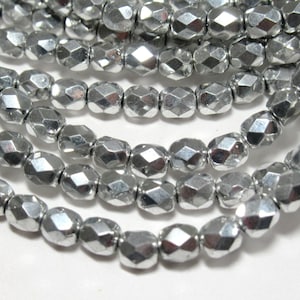 May include: Silver faceted glass beads, with a metallic finish. The beads are round and have a slightly elongated shape. They are strung together on a string.