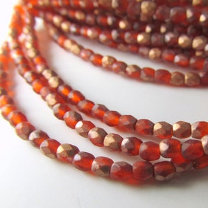 May include: A strand of red glass beads with a metallic gold finish. The beads are faceted and have a slightly irregular shape.
