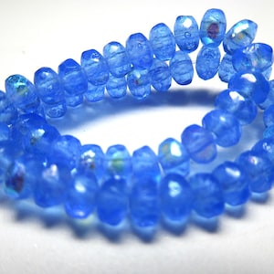 May include: A strand of iridescent blue glass beads. The beads are faceted and have a slightly irregular shape.