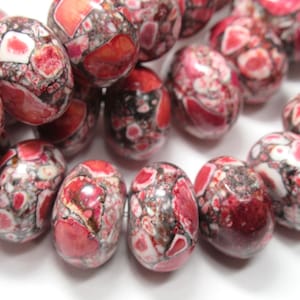 May include: A strand of oval-shaped beads with a speckled pattern of red, white, and black. The beads are made of a natural stone.