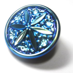 May include: A blue iridescent button with a raised, embossed design of a four-pointed star.