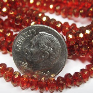 May include: A strand of red glass beads with a gold metallic finish. The beads are faceted and have a slightly irregular shape. A US dime is included for scale.