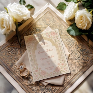 May include: Wedding invitation with floral design, featuring the names Amina Zahra & Omar Malik, and the date November 25. Two wedding rings and white roses are also visible. The invitation is on a patterned surface.