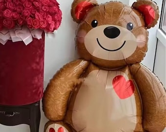 Può includere: Un grande palloncino a forma di orsetto marrone con un cuore rosso sul petto. L'orso ha accenti rossi sulle orecchie e sui piedi. Accanto all'orso, una scatola di velluto rosso piena di rose rosse.