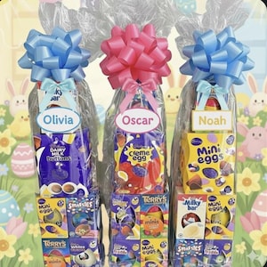 Può includere: Tre cesti regalo pasquali avvolti in cellophane trasparente, ciascuno sormontato da un grande fiocco. I cesti contengono dolcetti al cioccolato, tra cui Cadbury Dairy Milk Buttons, Creme Eggs e Mini Eggs. Ogni cesto ha un'etichetta con il nome.