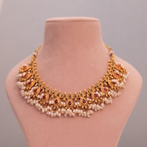 Könnte beinhalten: Eine weiße Keramiktasse mit schwarzem Henkel und dem Text "But First, Coffee" in fetter, schwarzer Schrift. Die Tasse steht vor einem verschwommenen Hintergrund, der eine gemütliche Umgebung suggeriert.