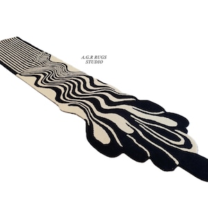 May include: A long, narrow runner rug featuring a high-contrast black and cream color scheme. The design displays linear patterns that transition into fluid, organic, wavy shapes. The text A.G.R RUGS STUDIO is printed in black on the cream section.