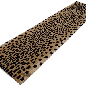 May include: A rectangular rug featuring a tan base with a pattern of black, irregular shapes. The rug has a soft, textured appearance. The bottom right corner of the rug has the text "A.G.R. ROOS STUDIO".
