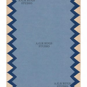 May include: A rectangular rug featuring a solid light blue center, a dark blue zigzag border, and a beige outer edge. The text A.G.R RUGS STUDIO is printed in gray at three different locations on the surface of the rug, including the top left, center, and bottom right.