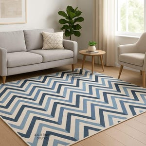 Puede incluir: Una alfombra rectangular con un diseño en zigzag en tonos azules y blancos. La alfombra está colocada sobre un suelo de madera en un salón, con un sofá gris, un sillón y una mesa auxiliar.