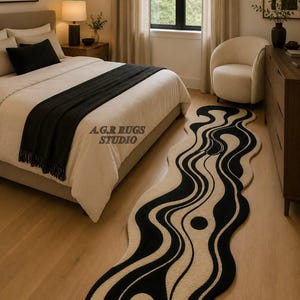 May include: An elongated, irregular-shaped area rug featuring a high-contrast black and cream wavy, abstract pattern with circular motifs. The text A.G.R RUGS STUDIO is visible on the rug surface. The rug has a textured pile and curved edges.