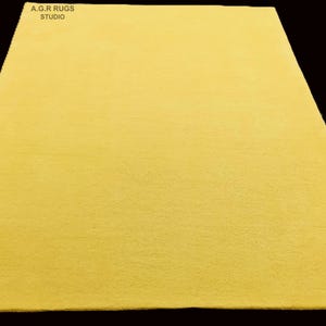 Op de afbeelding: Een rechthoekig, geel tapijt met een zachte textuur. Het tapijt wordt op een zwarte achtergrond weergegeven. De tekst "A.G.R RUGS STUDIO" is zichtbaar in de linkerboven- en rechterbenedenhoek.