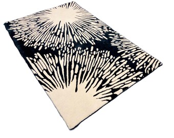 May include: A rectangular rug with a striking black and cream design. The pattern features a sunburst-like motif with radiating lines and speckled details. The rug's texture appears soft and inviting, suitable for a living space.