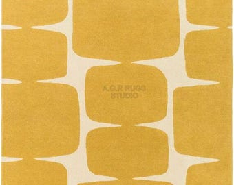 May include: Mustard yellow and cream-colored area rug with a repeating geometric pattern. The design features large, rounded rectangular shapes in mustard yellow against a cream background. The rug has the text "A.G.R RUGS STUDIO" in the corners.