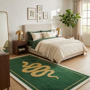 May include: A rectangular area rug featuring a deep green field with a central gold-colored coiled snake motif. The rug is bordered by a thin gold line and a thick cream-colored outer edge. The text A.G.R RUGS STUDIO is printed on the rug surface.