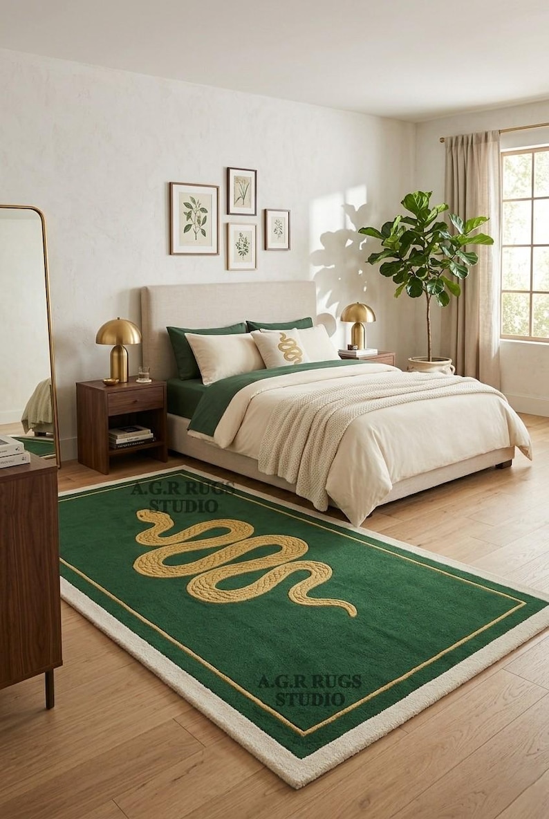 May include: A rectangular area rug featuring a deep green field with a central gold-colored coiled snake motif. The rug is bordered by a thin gold line and a thick cream-colored outer edge. The text A.G.R RUGS STUDIO is printed on the rug surface.