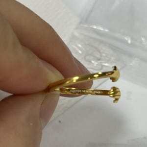 Puede incluir: Un anillo dorado con un dise&ntilde;o &uacute;nico. El anillo presenta dos manos estilizadas que parecen abrazarse. La inscripci&oacute;n "Hugs from me to you, always!!!" es visible en la banda del anillo.