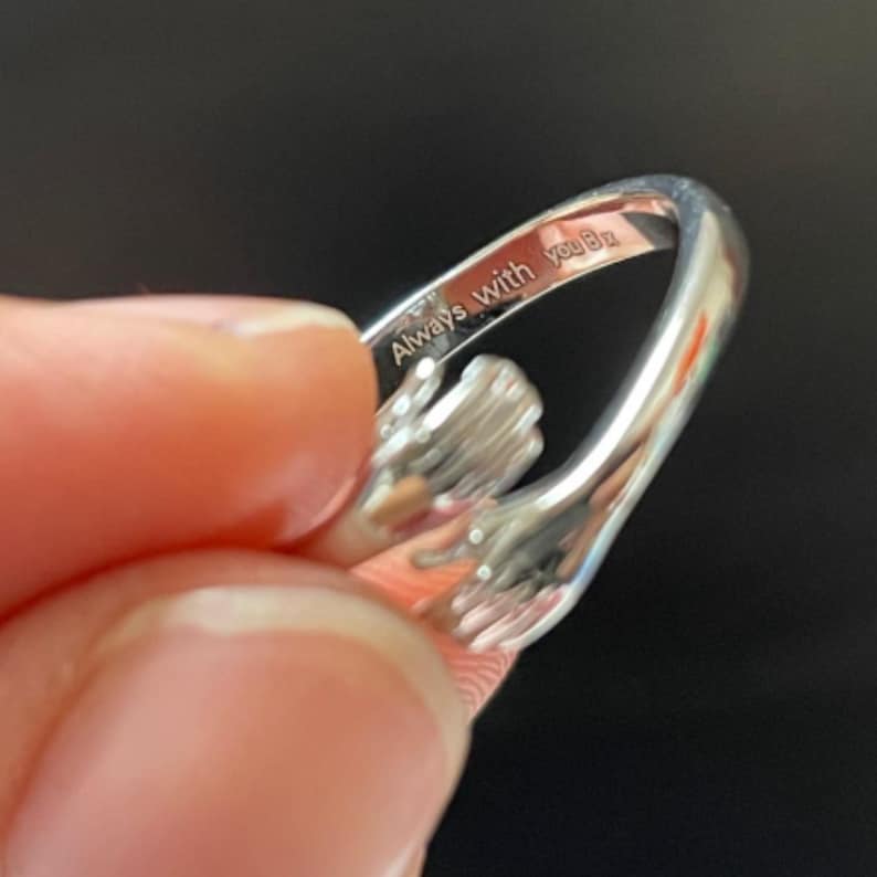 Puede incluir: Un anillo plateado con un dise&ntilde;o de manos abraz&aacute;ndose. El anillo tiene el texto grabado "Always with you". El anillo es una pieza de joyer&iacute;a.
