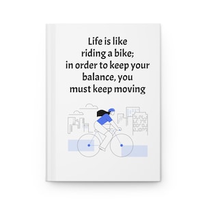 May include: White notebook with the text "Life is like riding a bike; in order to keep your balance, you must keep moving." A blue and white illustration of a person riding a bicycle is below the text.