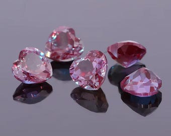 Può includere: Sei pietre preziose sfaccettate a forma di cuore, in varie tonalità di rosa e rosso, sono esposte su una superficie riflettente. Le gemme hanno molteplici sfaccettature che catturano la luce, creando un effetto scintillante.