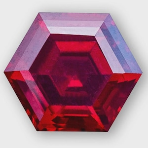 May include: A faceted, hexagonal gemstone with a deep red hue. The gem's surface reflects light, showcasing a complex internal structure with varying shades of red and hints of purple and blue. The overall shape is symmetrical and geometric.