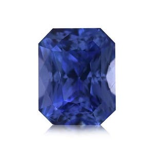 May include: A radiant, rectangular-cut sapphire gemstone. The gem is a deep, saturated blue color with multiple facets that reflect light. The sapphire is set against a white background, highlighting its brilliance.