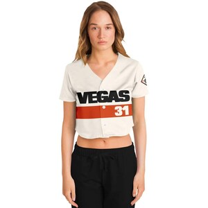 May include: Cream-colored cropped baseball jersey with the word "VEGAS" in black block letters above a red stripe. Below the stripe is the number "31" in white. A small logo is on the right sleeve.