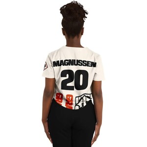 Op de afbeelding: Cr&egrave;mekleurig T-shirt met de naam "MAGNUSSEN" in zwarte blokletters boven het nummer "20". Het nummer is ook zwart. De onderkant van het shirt heeft een rood-zwart grafisch ontwerp. Het shirt heeft korte mouwen.