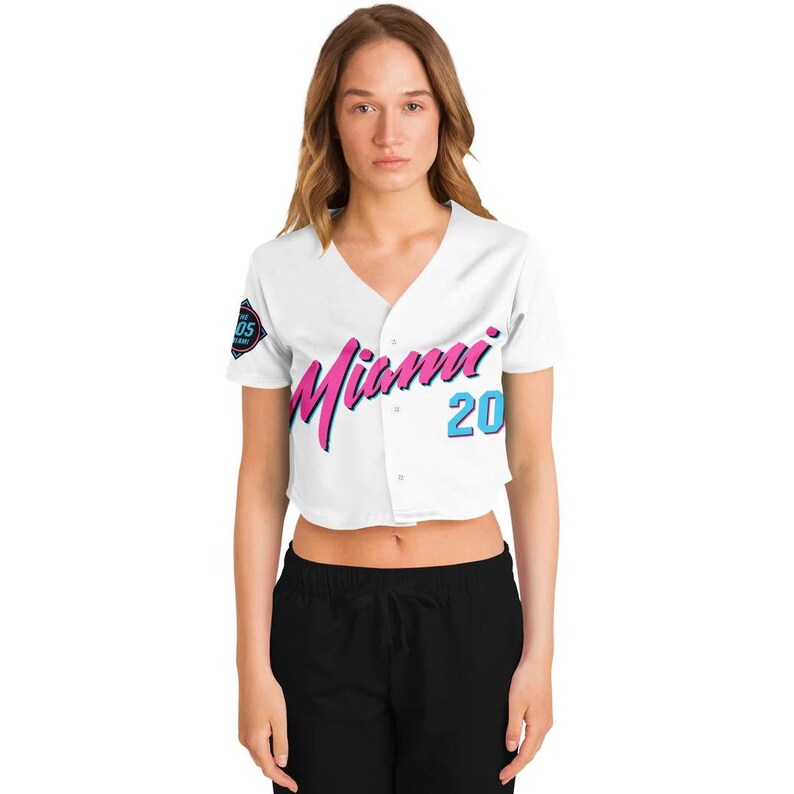 Peut inclure: Un maillot de baseball blanc court avec le mot "Miami" en script rose et bleu sur le devant. Le num&eacute;ro "20" est en bleu. Un petit &eacute;cusson est sur la manche gauche. Le maillot a un col en V et une fermeture &agrave; boutons.