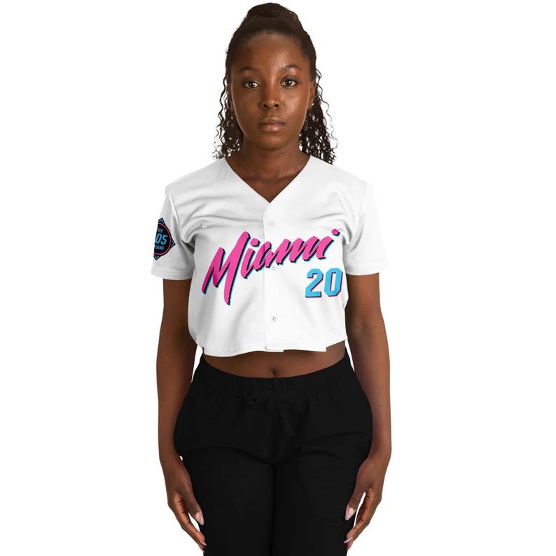 Peut inclure: Maillot de baseball blanc avec le mot "Miami" en script rose et bleu sur la poitrine, ainsi que le num&eacute;ro "20" en bleu. Le maillot a un col en V et des manches courtes. Un &eacute;cusson est visible sur la manche gauche.