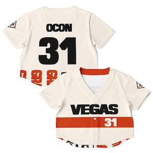 May include: Cream-colored baseball jersey with black lettering and the number 31. The jersey has a red stripe across the chest with the word "VEGAS" in black. A small logo is on the sleeve.