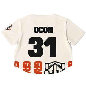 May include: Cream-colored baseball jersey with the name "OCON" and the number "31" in black. The bottom hem features a repeating pattern in red and black. A small patch is visible on the left sleeve.