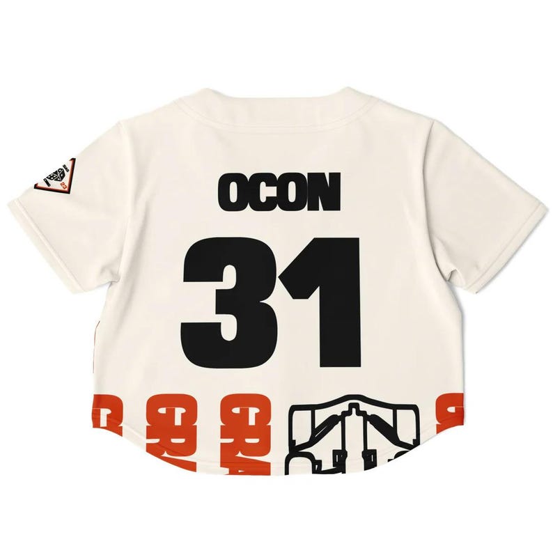 May include: Cream-colored baseball jersey with the name "OCON" and the number "31" in black. The bottom hem features a repeating pattern in red and black. A small patch is visible on the left sleeve.