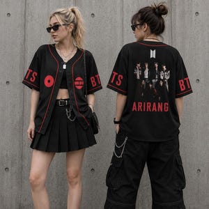 Peut inclure: Deux personnes portant des maillots de baseball noirs avec des accents rouges et les lettres "BTS". L'une porte une jupe plissée noire, l'autre un pantalon cargo noir. Les deux portent des baskets noires et blanches. Les maillots ont le mot "ARIRANG" au dos.